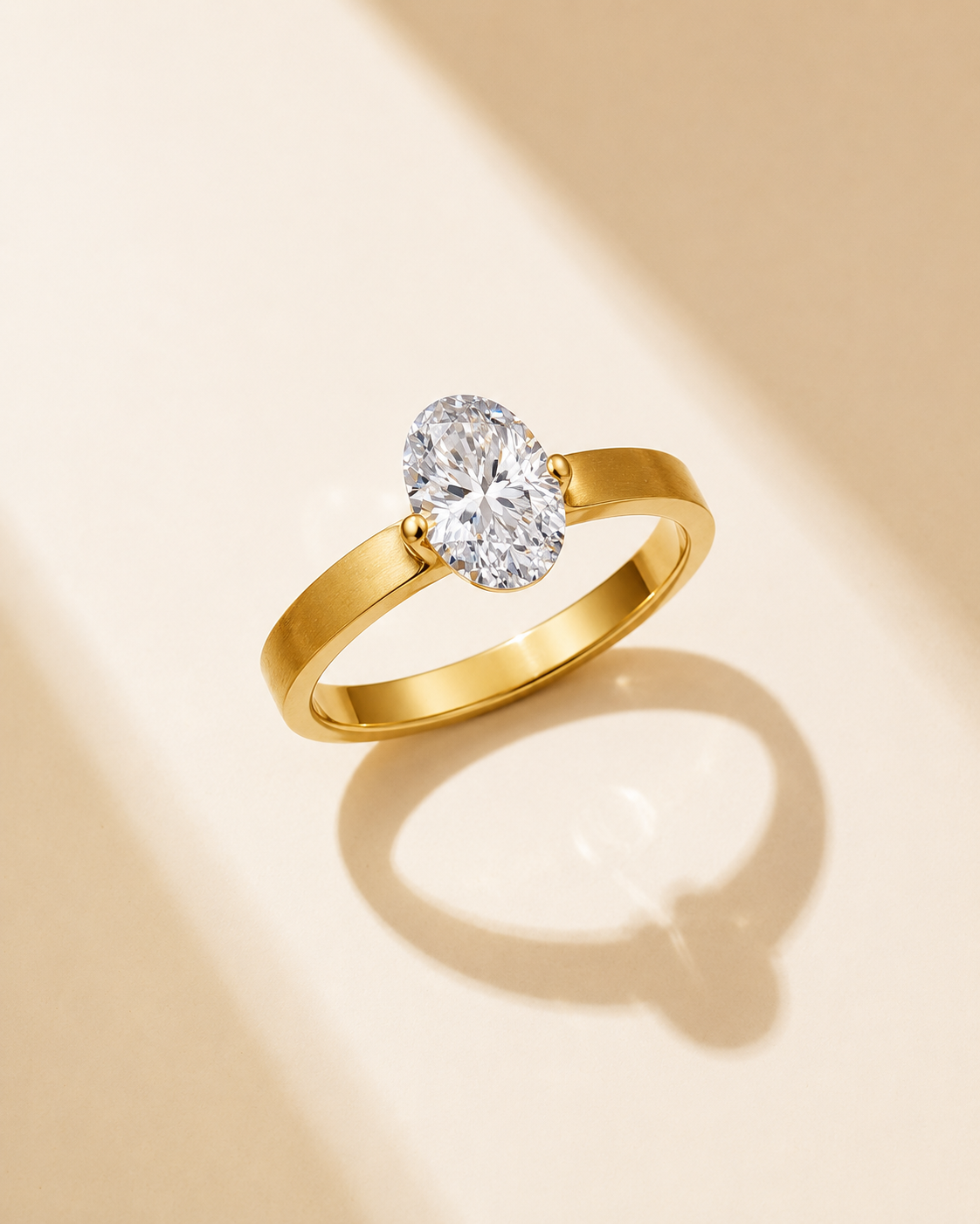 Gold solitaire ring with oval clear stone on warm beige background with soft shadow.
