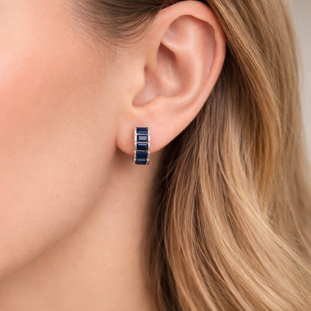 Close-up of an ear wearing a blue hoop earring with blonde hair.