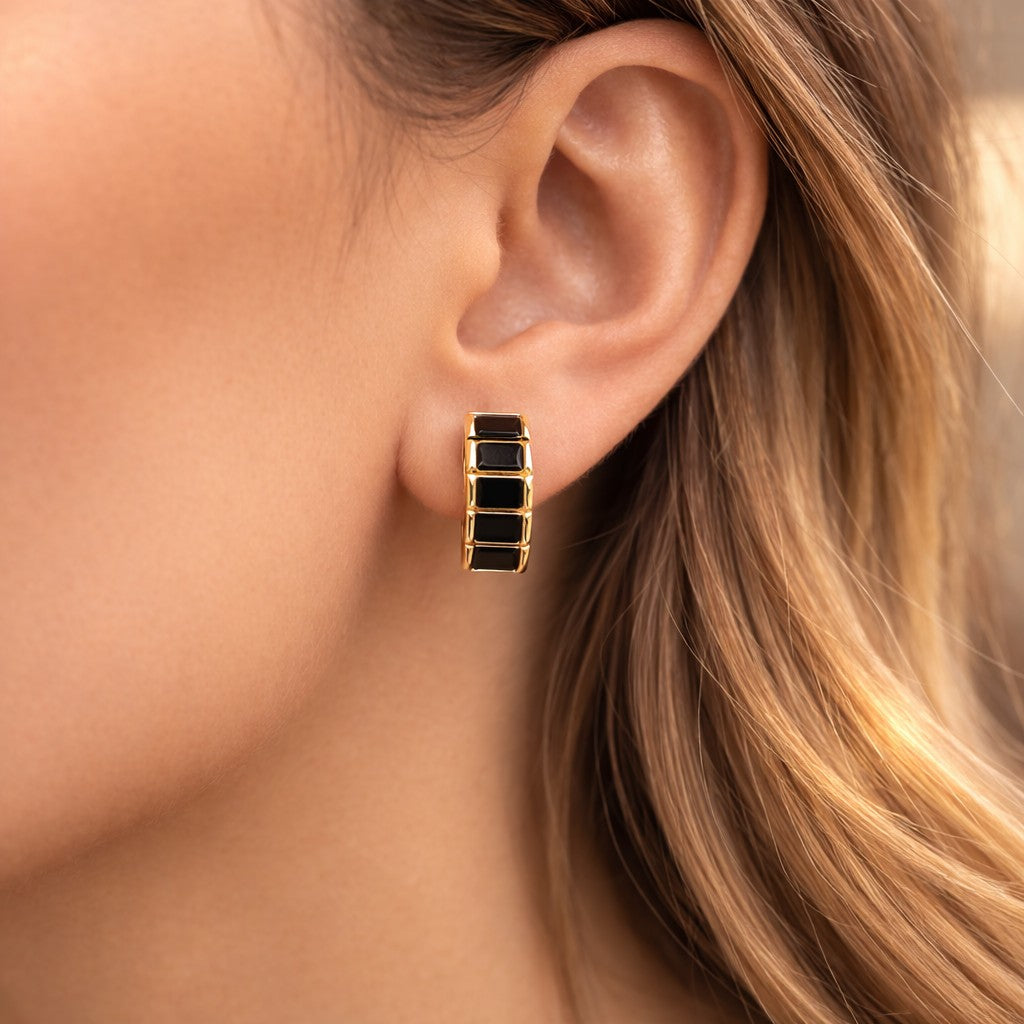 Gold hoop earrings with black stones worn by a person with blonde hair.