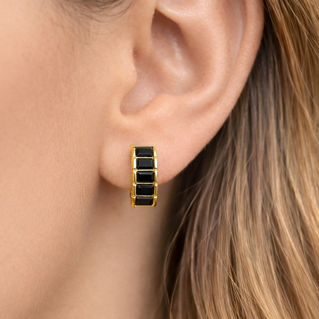 Close-up of an ear wearing a gold hoop earring with black stones.