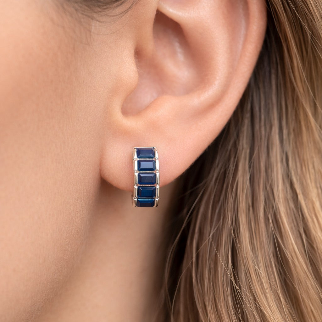 Close-up of an ear wearing a blue square hoop earring.